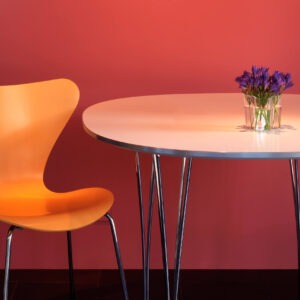 Orange designerstol ved et bord op ad en rød væg.